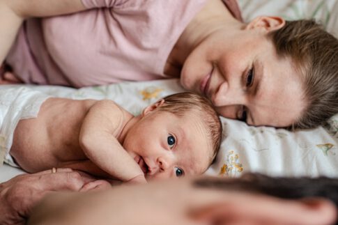 Mutter liegt lächelnd neben Baby bei einem Familienshooting. Neugeborenen Fotografie in Celle