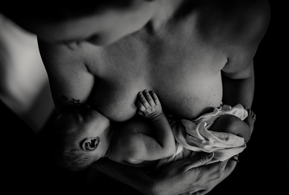 Mutter stillt ihr Neugeborenes in schwarz weiß. Stillfotografie Celle