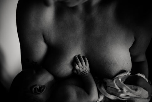 Fotografie Stillen Newbornshooting in schwarzweiß. Die Mutter stillt ihr Neugeborenes von Oben fotografiert.