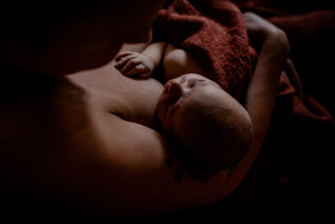 Fotografie eines Wochenbettshootings. Baby schläft nach dem Stillen auf dem Arm seiner Mutter