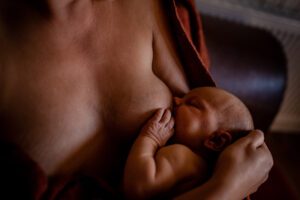 Still- und Tragebild Beim Stillen hält das Neugeborene sein Händchen auf der Brut der Mutter.