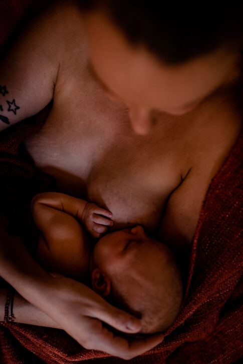 Neugeborenes nach dem Stillen an Mamas Brust. Die Mama hält zärtlich das Köpfchen.