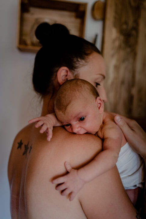 Fotografie Stillen Newbornshooting. Neugeborenes nach dem Stillen an der Schulter der Mutter zum Bäuerchen.
