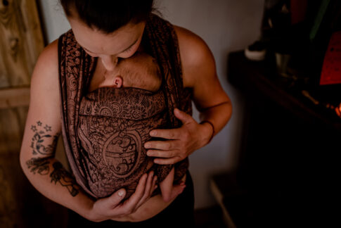 Tragetuchfotografie die Mama trägt ihr Baby während des Shootings im Tuch und küsst zärtlich den Kopf ihres Babys.