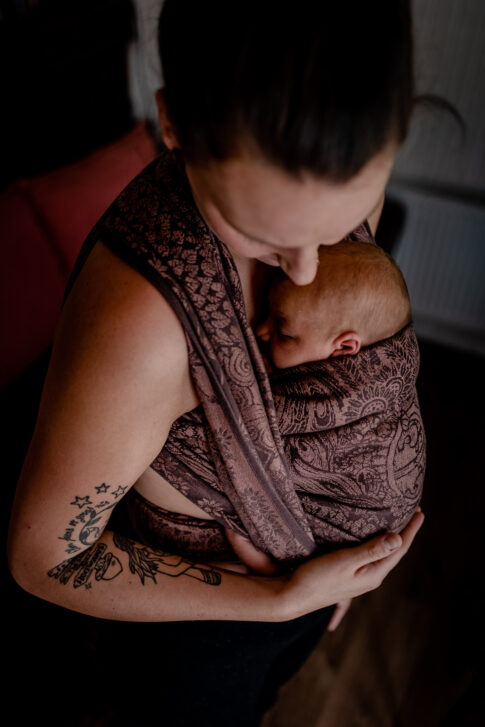 Tragebild hochkant die Mutter schaut liebevoll auf ihr Baby im Tragetuch beim Neugeborenen Shooting in Celle.