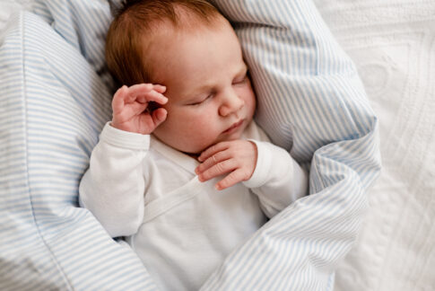 Neugeborenes liegt auf einem hellblau- weiß gestreiften Kissen. Es hat die die Augen geschlossen. Fotografie eines Newbornshootings in Hannover.