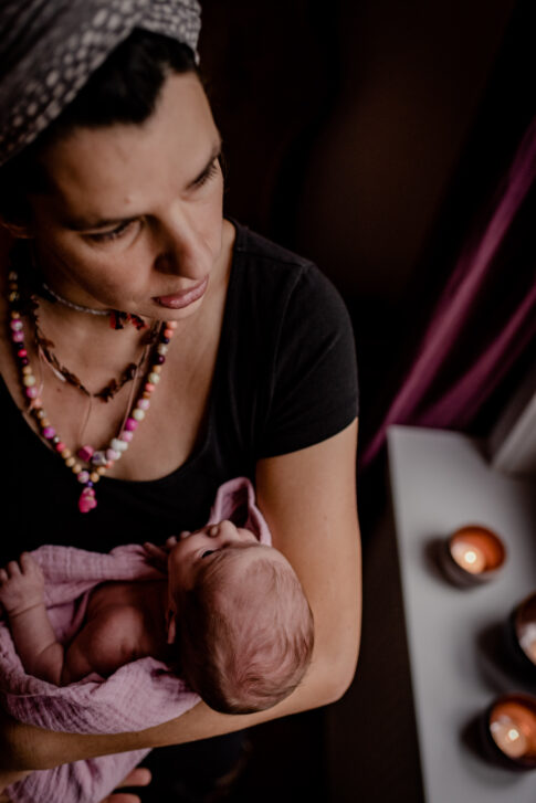 Mutter mit Neugeborenen auf Arm schaut aus dem Fenster in Geburtsräumen von Wiebke Niemann