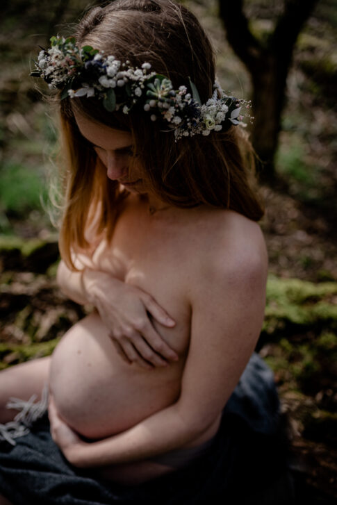 werdende Mutter mit Blumenkranz im Haar beim Babybauchshooting in der Natur in Celle