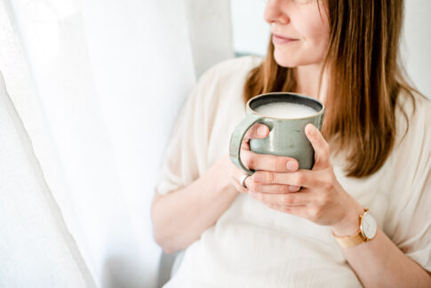 Frau hält Kaffeebecher in der Hand und schaut entspannt aus dem Fenster. Man erkennt sie nicht. Businessfotografie Celle