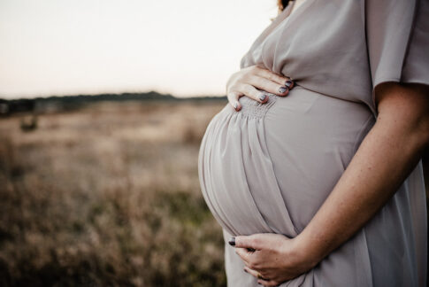 Babybauch vor Wiese im Kleid während eines Schwangerschaftsshooting in Wolfsburg