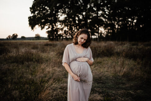 werdende Mutter im rosa Kleid während Schwangerschaftsshooting auf Wiese in Wolfsburg