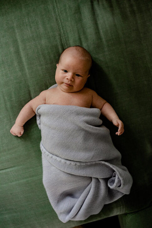 Neugeborenes liegt in Decke gewickelt auf grünem Sofa