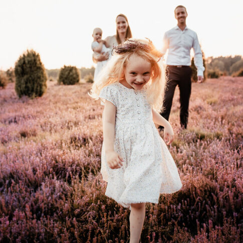 kleines Mädchen rennt vor Eltern auf die Kamera zu bei Familienshooting in der Misselhorner Heide
