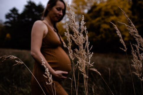 Gräser im Vordergrund. im Hintergrund schwangere Frau bei Babybauchfotografie in Celle