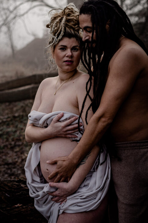 Schwangere Frau mit Partner in mystischer Atmosphäre am Wasser. Beide haben Dreadlocks .