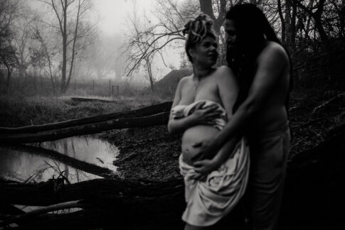 Schwangere Frau und Partner in schwarzweiß, beide sind unscharf. im Hintergrund erkennt man Wasser und Nebel