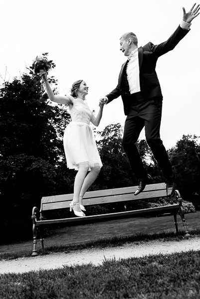 Witziges Brautpaarshooting, lustiges Hochzeitsfoto Brautpaar springt von Parkbank vor dem Kloster Wienhausen bei Celle