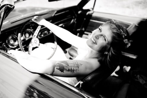 Braut lässig mit Tattoos am Fahrersitz des Brautautos, während der Brautpaarfotos in Celle