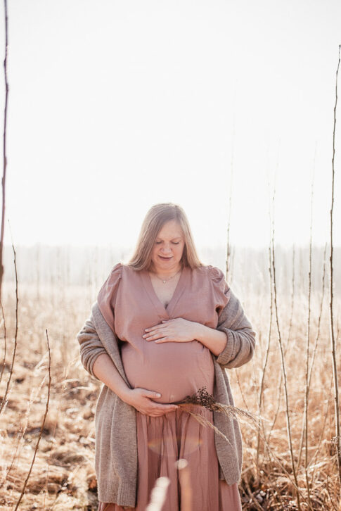 Schwangere Frau auf Morgennebel bedeckter Wiese bei Babybauchshooting in Celle