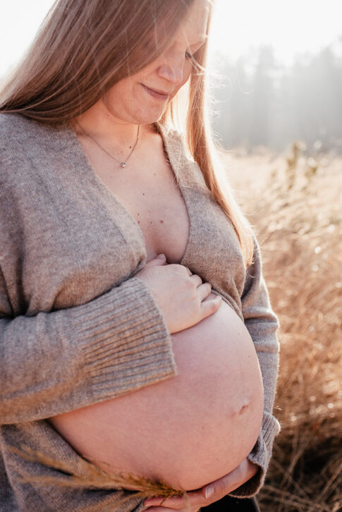 Schwangere Frau nur mit Cardigan bedeckt bei Babybauchshooting auf einer Wiese Bei Celle