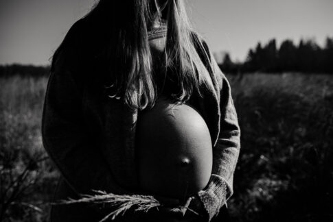 Kontrastreiches Bild in Schwarzweiß von einer Schwangeren auf Wiese