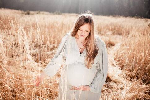 schwangere Frau geht in mintfarbenden Kleid über helle beige Wiese bei Babybauchshooting in Celle