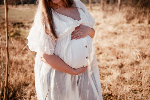 schwangere Frau in weißem Shootingkleid bei Babybauchshooting auf einer Wiese bei Celle